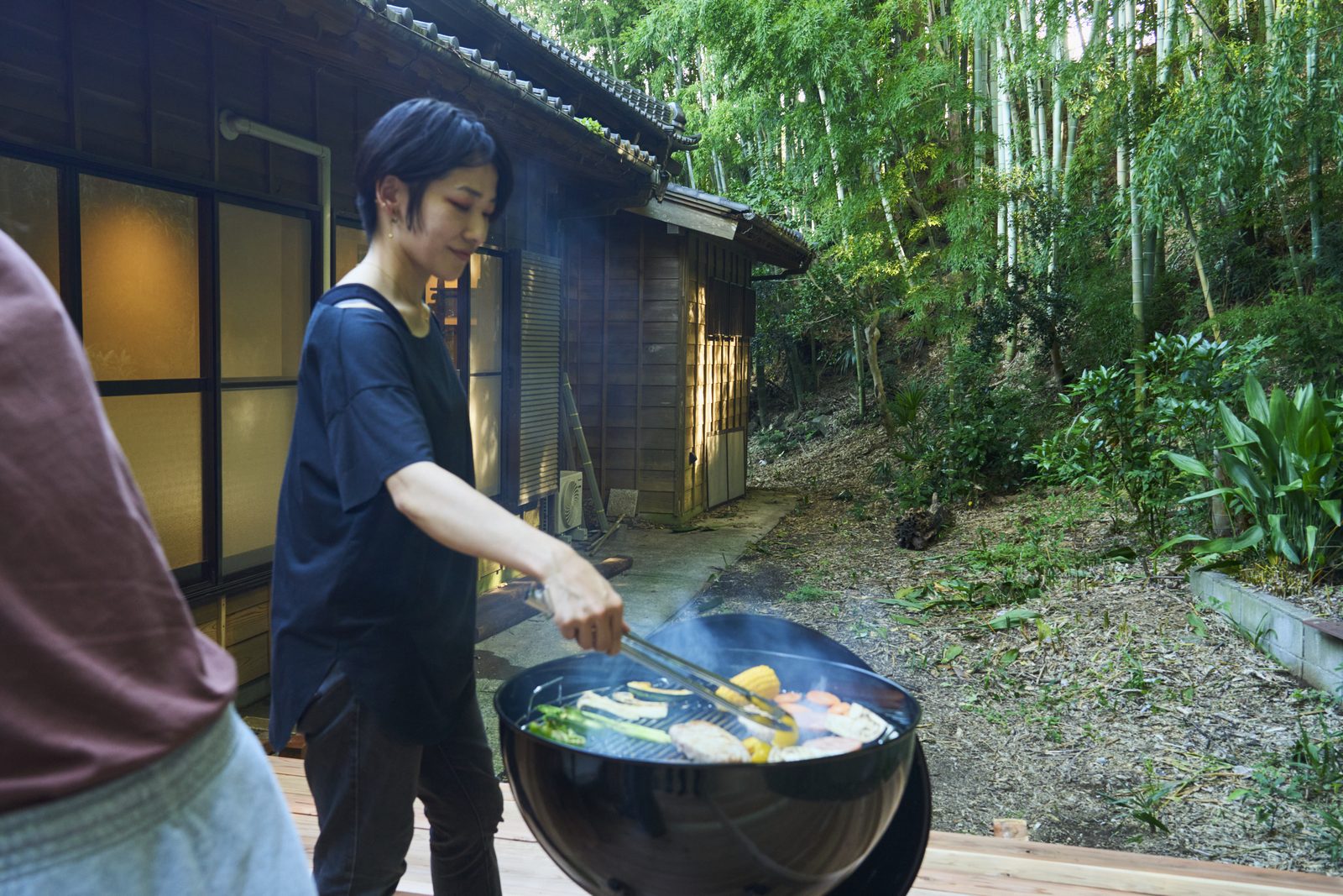 竹林を背に、炭火で野菜と肉を焼く滞在者